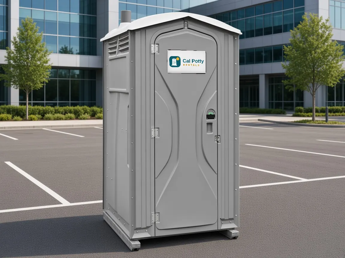 A grey porta potty in an office parking lot in front of a glass building, an example setup for porta potty rental in Cupertino
