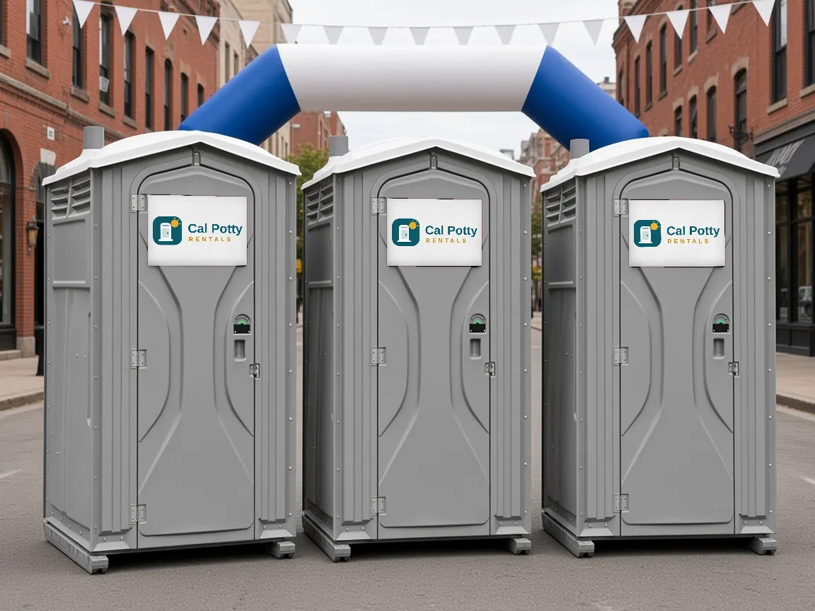 Three grey portable toilets on a downtown street under a blue and white inflatable arch
